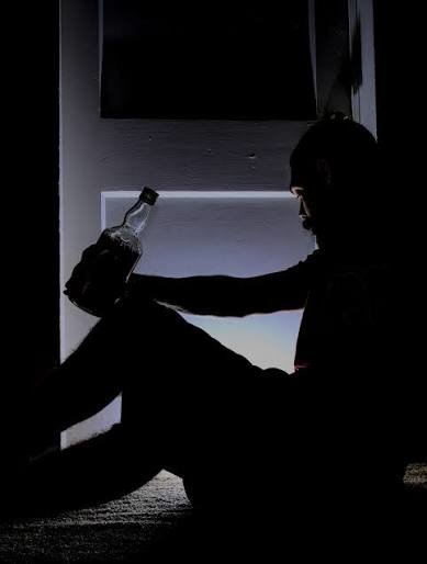 imagem de homem sentado no escuro com garrafa de bebida na mão